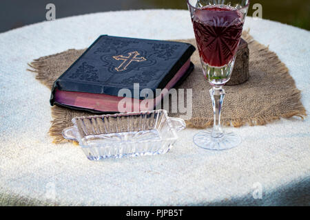 Tenendo la comunione. Bicchiere di vetro con il vino rosso, il pane e la Santa Bibbia sul tavolo di legno di close-up. Foto Stock