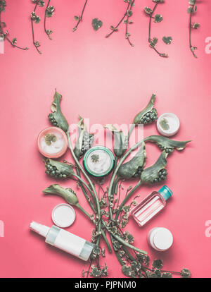 Concetto di bellezza con vari viso prodotti cosmetici con mock up, foglie e fiori di colore verde sul rosa pastello lo sfondo del desktop. Moderno di cura di pelle formato Foto Stock