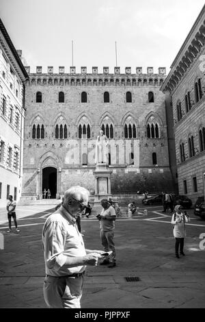 Le persone sono la lettura di notizie sui giornali e telefono cellulare nella parte anteriore del Monte dei Paschi di Siena Banca Mps. foto in bianco e nero Foto Stock