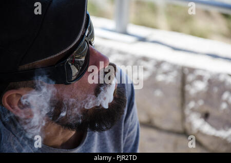 Uomo con occhiali da sole soffiò il fumo dalla sua bocca bassa tecnica chiave Foto Stock