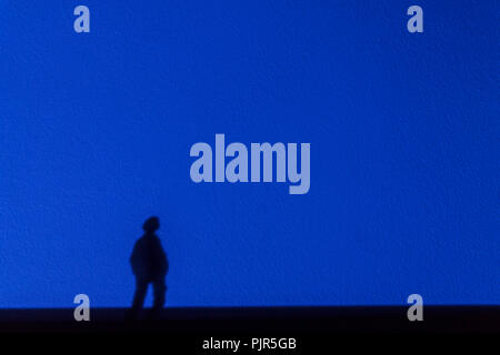 Silhouette dalle ombre di un solitario uomo sognante fissando in distanza su di una parete di blu. Il concetto di solitudine, di sogno e romanticismo. Foto Stock