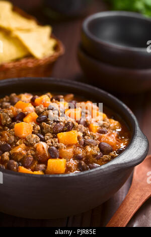 In casa chili con carne con carne macinata, rosso e i fagioli neri, la salsa di pomodoro e zucca in ciotola rustico con tortilla chips nel retro Foto Stock