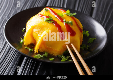 Ricetta per la frittata giapponese con riso, pollo, verdure e salsa di pomodoro su una piastra nera su una tavola di legno orizzontale. Foto Stock