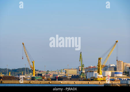 Tre gru pesanti e due per il giallo e uno verde utilizzato per il caricamento di navi mercantili nel porto di La Coruna in Spagna Foto Stock