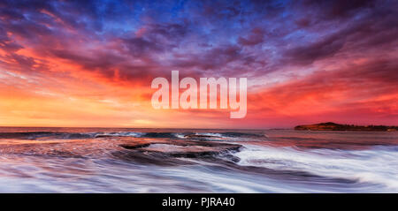 Colorato cloudscape illuminato da Rising Sun più tempestose onde del Pacifico di rotolamento cloud intorno a Mona Vale rock pool rocce di arenaria e la spiaggia. Foto Stock