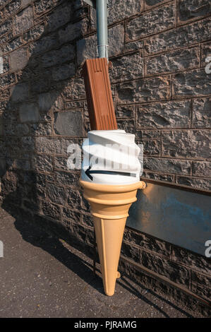 Un giudiziosamente collocati in plastica grandi ice-cream cornet con una barra di cioccolato fissato ad un cartello contro una piastra di metallo su un caratteristico muro di pietra Foto Stock