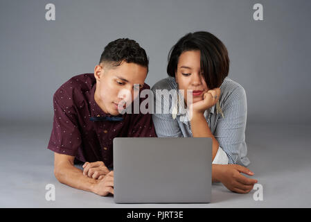 Annoiato coppia giovane guarda il filmato sul computer portatile isolato su grigio di sfondo per studio Foto Stock