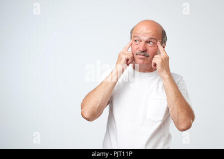 Ritratto di isolato di perplesso maschio senior cercando e tenendo le dita sul suo templi, cercando di ricordare qualcosa Foto Stock