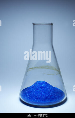 Blu brillante cristalli in un heap, brilla sul fondo del matraccio di Erlenmeyer. dark tinta ciano di sfondi Foto Stock