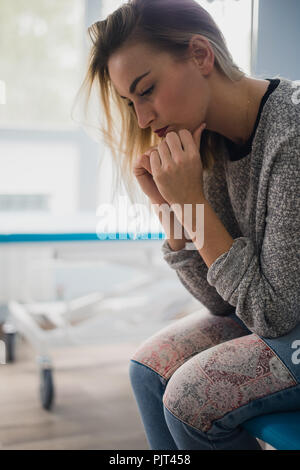 Una donna sedersi sul letto di un ospedale con ansia. Aveva paura di disperazione che cosa lei vuole ora è la fede e la morale. Foto Stock