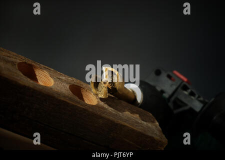 Punta per cerniera per la perforazione di fori circolari con un trapano portatile seduti sulla parte superiore del blocco di legno su sfondo nero Close up libero spazio di copia Foto Stock