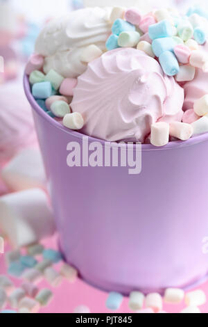 Violetta secchio con vari marshmallows su uno sfondo di colore rosa. Foto Stock