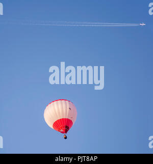 Jet aereo con lungo sentiero bianco vola sopra una mongolfiera in un bel cielo azzurro Foto Stock