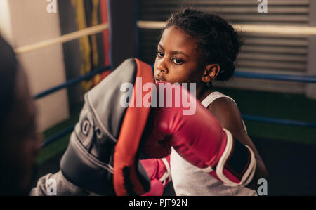 Close up di un capretto formazione all'interno di un anello di inscatolamento. Kid boxer indossando guanti da boxe praticando punzoni su un tampone di punzonatura. Foto Stock