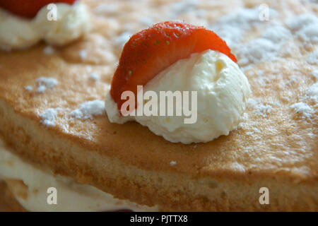 Un segmento di fragola su un ciuffo di panna montata. Sulla sommità di uno strato di pan di spagna con panna e macrons. Una glassa di zucchero fine sulla torta. Foto Stock