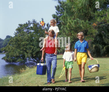 1990 STORICA FAMIGLIA NUCLEARE CAUCASICA TRADIZIONALE CHE CAMMINA INSIEME ALL'ESTERNO IN UN PICNIC SUL LAGO Foto Stock