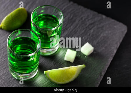 Due bicchieri di assenzio con fettine di lime e pezzi di zucchero su uno sfondo scuro Foto Stock