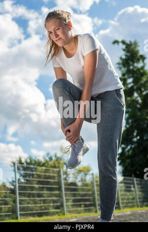 Giovane donna runner tenere il suo sport gamba ferita con una faccia painfull Foto Stock