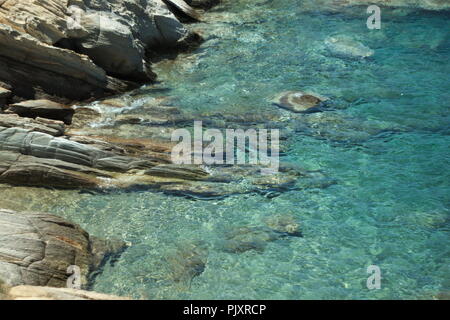 Le acque cristalline del Mar Egeo, nella baia di Mylopotos, sulla splendida isola greca di iOS. Le onde lambiscono delicatamente sulle rocce Foto Stock