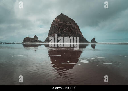 La Haystack Rock a bassa marea su un giorno nuvoloso con la riflessione sulla riva, famoso mare pila di Oregon Coast, Cannon Beach, Stati Uniti d'America. Foto Stock