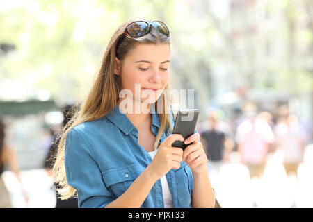 Rilassata donna usa un telefono intelligente a piedi in strada di una grande città Foto Stock