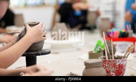 Gli studenti che lavorano con argilla ottenere le loro mani sporche. Arte Visiva di classe che mostra le mani su una bobina pot con argilla tols e scrivania in background. Arte educatio Foto Stock