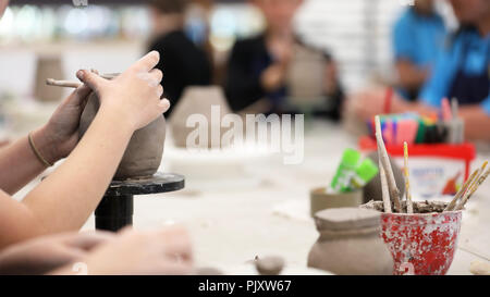 Gli studenti che lavorano con argilla ottenere le loro mani sporche. Arte Visiva di classe che mostra le mani su una bobina pentola con strumenti di argilla e scrivania in background. Arte educazione Foto Stock