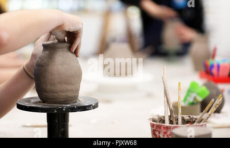 Gli studenti che lavorano con argilla ottenere le loro mani sporche. Arte Visiva di classe che mostra le mani su una bobina pentola con strumenti di argilla e scrivania in background. Arte educazione Foto Stock