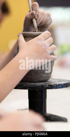 Gli studenti che lavorano con argilla ottenere le loro mani sporche. Arte Visiva di classe che mostra le mani su una bobina pentola con strumenti di argilla e scrivania in background. Arte educazione Foto Stock