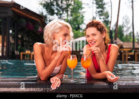 Felice di giovani donne a bere gustosi cocktail in piscina Foto Stock