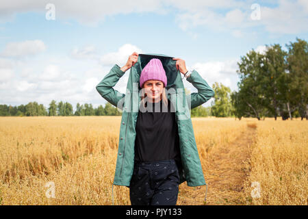 Giovane donna nel manto verde, maglia hat, jeans passeggiate, godersi la natura e la luce del sole in campo di paglia. Concetto di vacanze autunnali presso il Village e live Foto Stock