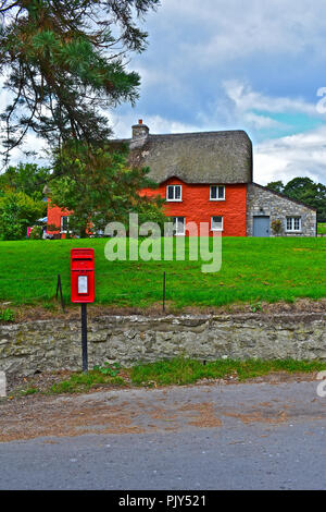 Un bel dipinto di rosso cottage in pietra con tradizionale tetto in paglia, nella rurale villaggio gallese di Merthyr Mawr, nei pressi di Bridgend, nel Galles del Sud Foto Stock