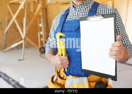 Lavoratore con una chiave inglese e appunti alla costruzione di sito Foto Stock