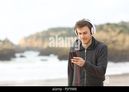 Teen rilassati ascoltando la musica con le cuffie e un telefono intelligente di camminare sulla spiaggia Foto Stock