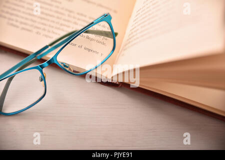 Dettaglio di occhiali sul libro aperto sul tavolo bianco .concetto bisogno di occhiali per leggere. Vista dall'alto. Composizione orizzontale Foto Stock