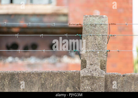 Una vista ravvicinata di linee di filo spinato attaccato ad un muro di cemento intorno a un edificio abbandonato Foto Stock