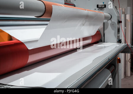 Grande stampa professionale laminatore, armati con rossi grandi rotoli di carta lucida e piccoli tubi di pellicola trasparente. Foto Stock