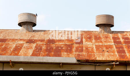 Metallo due aeratori su un vecchio arrugginito in acciaio del tetto di un edificio abandened con una grondaia danneggiato Foto Stock