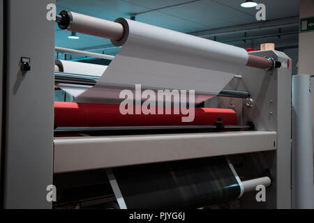 Grande stampa professionale laminatore, armati con rossi grandi rotoli di carta lucida e piccoli tubi di pellicola trasparente. Foto Stock
