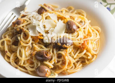 Spaghetti con le acciughe, capperi e olive nere close up conditi con formaggio parmigiano trucioli Foto Stock