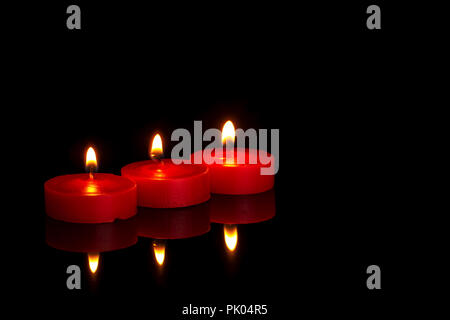 Tre piccole candele rosse, tealight, la masterizzazione di notte sul nero. In memoriam o forse religiosa. Foto Stock