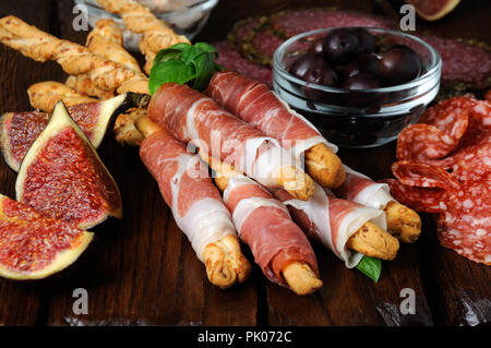 Piatto per antipasti spuntini grissini avvolti con prosciutto (Grissini) con salame, olive sulla superficie di legno Foto Stock