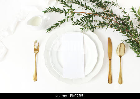 Nozze di festa di compleanno, messa in tavola con posate dorate, eucalyptus parvifolia branch, piastra di porcellana, latte e nastro di seta. Scheda vuota mockup. Ristorante rustico concetto di menu. Piatto, laici vista superiore Foto Stock