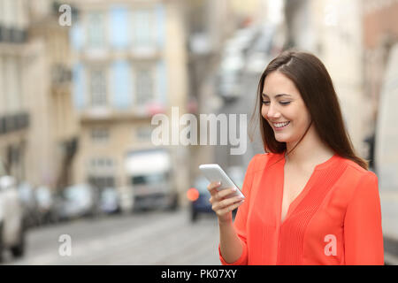 Donna felice in arancione utilizza un telefono intelligente a piedi in strada Foto Stock