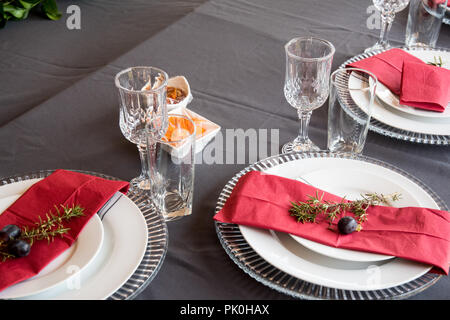 Un tavolo pranzo insieme con sotto le piastre, grazioso grigio e le piastre bianche, rosso salvietta, decorativo piccolo ramo di albero, due uve con motivi floreali e decorazioni di frutta Foto Stock
