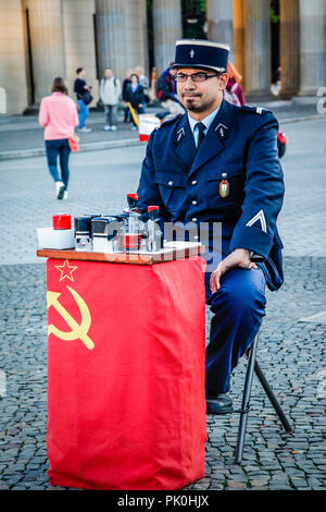 Uomo vestito da una gendarmeria francese si siede vicino alla Porta di Brandeburgo che offrono souvenir guerra fredda passa per le persone che visitano Berlino Foto Stock