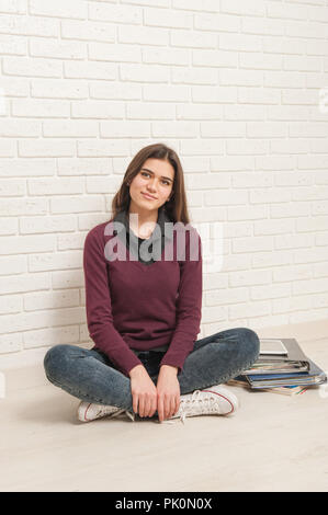 Una studentessa seduta sul pavimento contro un muro di mattoni Foto Stock