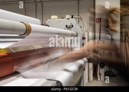 Grande stampa professionale laminatore, armati con rossi grandi rotoli di carta lucida e piccoli tubi di pellicola trasparente. Foto Stock