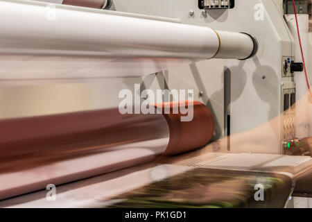 Grande stampa professionale laminatore, armati con rossi grandi rotoli di carta lucida e piccoli tubi di pellicola trasparente. Foto Stock
