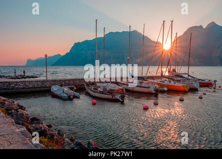 Barche al molo durante il tramonto sul Lago di Garda. Tramonto sulla Riva del Garda. Il sole tramonta in montagna. Il lago nel nord Italia. Foto Stock